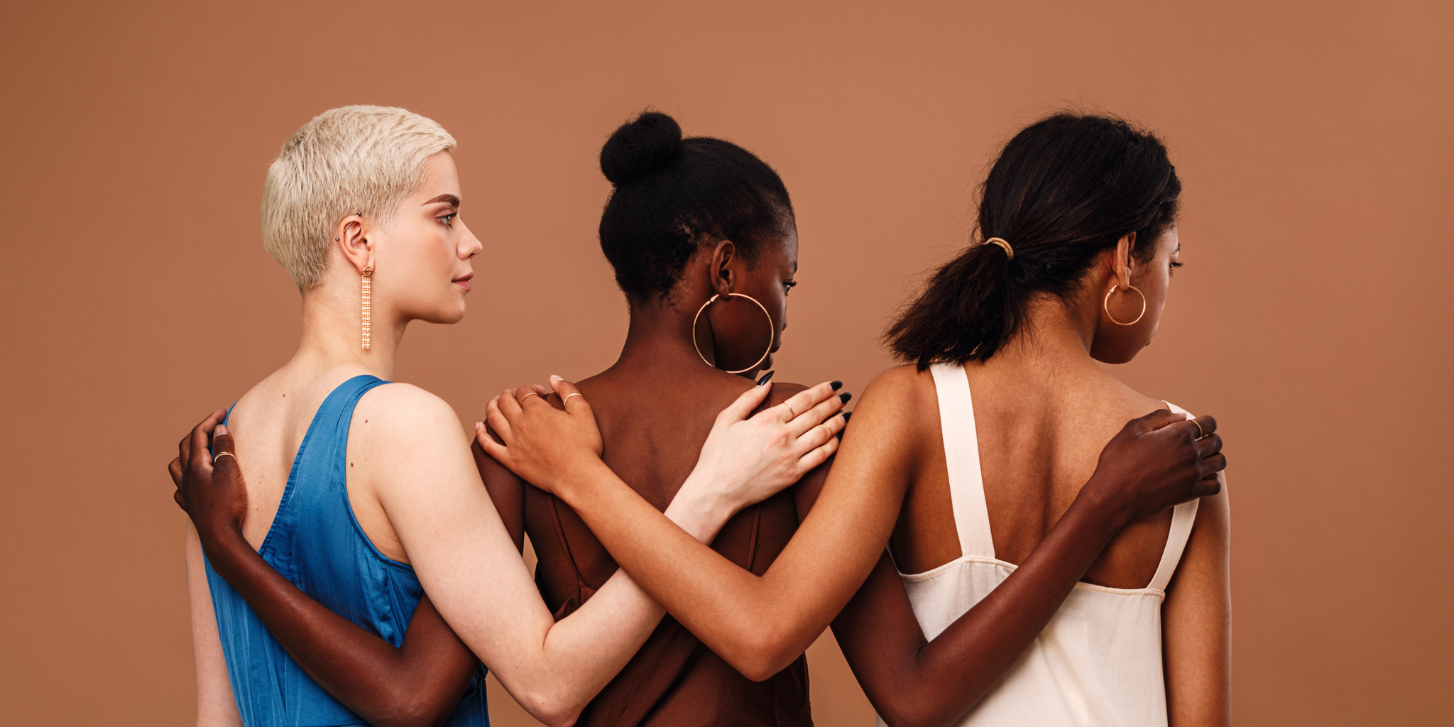 3 Frauen mit verschiedenen Haut und Haarfarben halten ihre Hände hinter ihren Rücken zusammen, um Menstruation in verschiedenen Kulturen darzustellen.