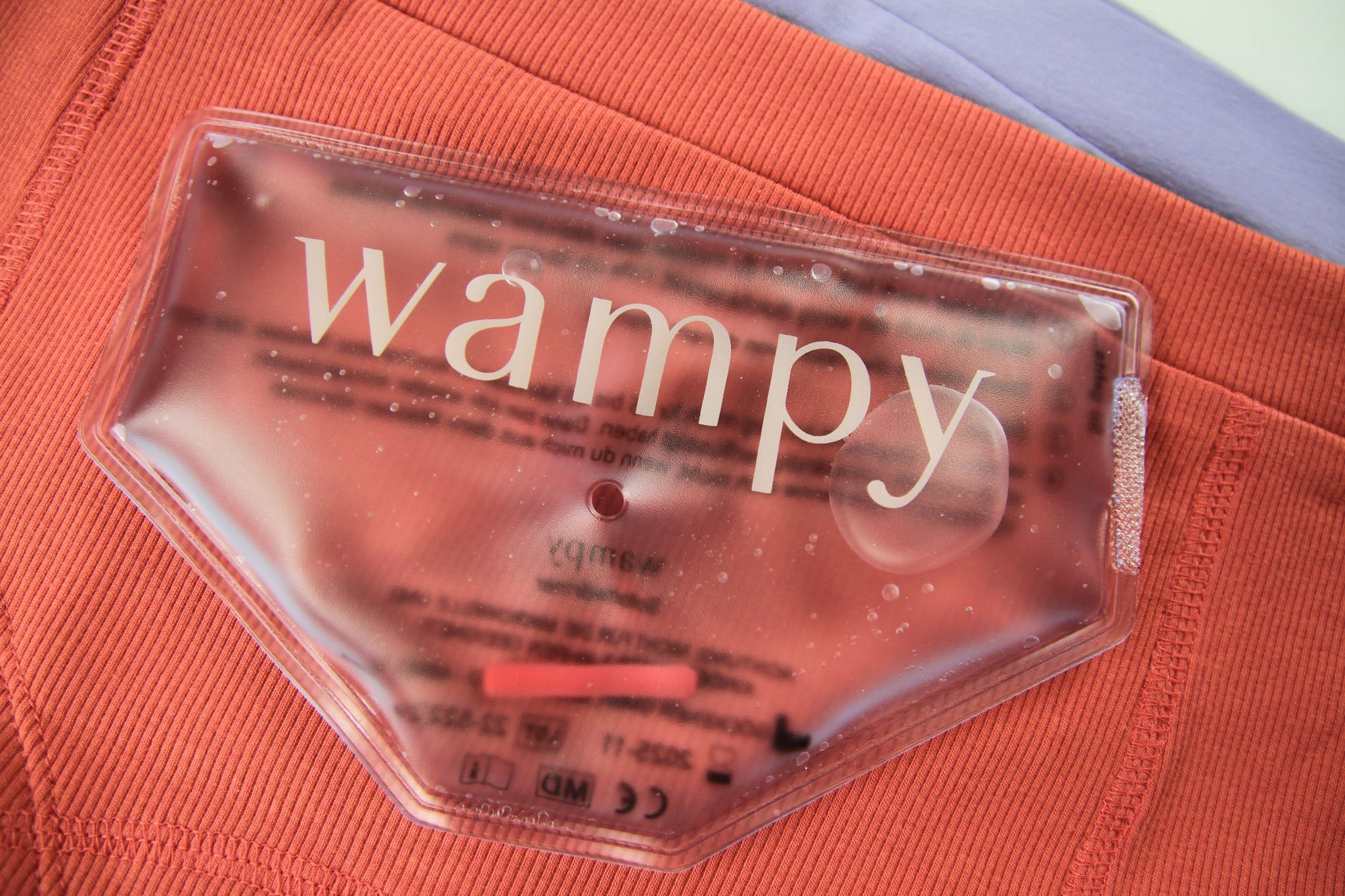 Ein Wampy Wärmepad auf rosaroter und lavendel Unterhose. Beheizbare Unterwäsche gegen Menstruationsschmerzen.
